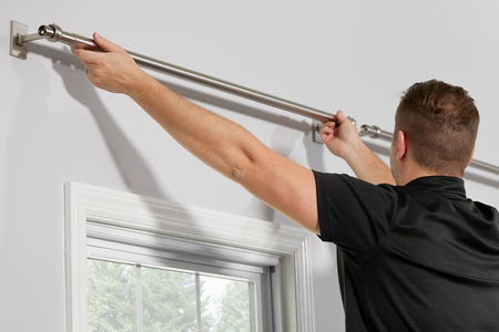 A man attaches a curtain rod to a wall.